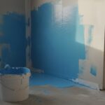 enduit étanchéité sous carrelage douche - application au rouleau d'une protection à l'eau bleue sur le mur d'une douche